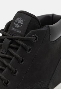 Zwarte Timberland schoenen met een textuur in suède, ronde veters, metalen oogjes en een gewatteerde kraag. Logo zichtbaar op de tong.