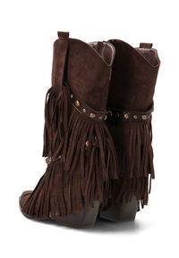 Botines de ante marrón con flecos largos, tachuelas decorativas de metal, punta abierta y tacón ancho, diseñados para una estética bohemia.