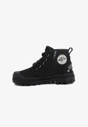 Baskets montantes en toile noire avec zip latéral, lacets noirs, semelle robuste et patch circulaire blanc sur la cheville.