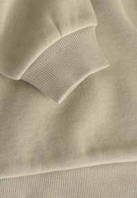 Tessuto di felpa beige chiaro con polsini a costine. Texture morbida, design casual e dettagli di cucitura senza giunti lungo i bordi.