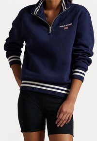 Navy blue fleece half-zip pullover with white stripes on the collar and cuffs; features "POLO SPORT" logo and a smooth texture.