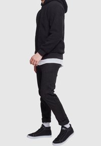 Czarna polarowa bluza z fakturowym wykończeniem, zestawiona z czarnymi zwężającymi się spodniami i czarnymi wysokimi trampkami z białymi podeszwami i akcentami.