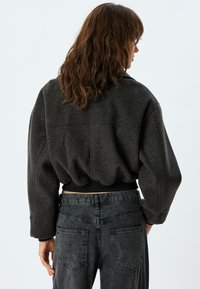 Donkergrijze, kortere jas met een gestructureerde afwerking, voorzien van een geribde zoom en wijde mouwen, gecombineerd met faded zwarte high-waisted jeans.