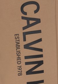 Beige bavlněná mikina s velkým černým nápisem "CALVIN" a "ESTABLISHED 1978" potisknutým kolmo po jedné straně.