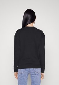 Felpa nera con girocollo, spalle scese e polsini a coste, abbinata a jeans azzurri chiari. Design semplice, senza motivi o accenti.