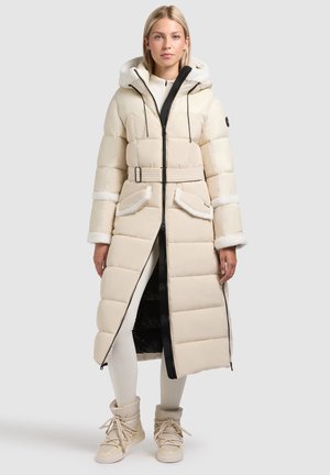 Padded dugi kaput u bež boji s patentnim zatvaračem sprijeda, kapuljačom, remenom i rukavima obloženim krznom. Ima dva prednja džepa i kontrastnu unutarnju podstavu.
