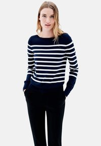 Pull long à rayures bleu marine et blanc, avec un col rond et des poignets côtelés, associé à un pantalon noir. Texture douce, coupe décontractée.