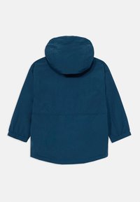 Veste légère bleu marine avec capuche, poignets élastiques et coupe décontractée. Caractéristiques incluent une texture lisse et un design de longueur intermédiaire.
