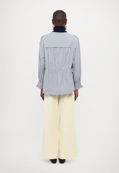 Striped shirt jacket in light blue with gathered back, long sleeves, and elastic cuffs, paired with wide-leg cream pants.