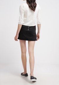 Top bianco con maniche in pizzo, mini gonna nera e calzature nere con suola bianca, che mostrano uno stile semplice e moderno.