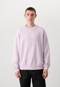 Lilac krēklis ar ribotu apkakli un piedurknēm, uz priekšpuses izšūts "HUGO" logo, ar brīvu piegriezumu un teksturētu audumu.