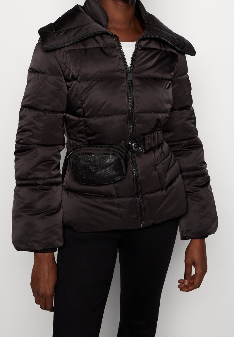 Osoba ubrana w czarną pikowaną kurtkę z dużym kołnierzem, zamkiem z przodu, paskiem z klamrą oraz przymocowaną małą czarną saszetką wokół talii.