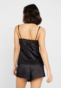 Melnais satīna krekliņš un šortiem komplekts, ar smalku mežģīņu apdari ap kakla izgriezumu un apakšmalu, ar regulējamiem siksniņām un gludu tekstūru.