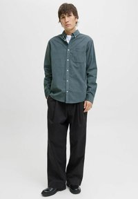 Mørkegrønn skjorte med knapper og lomme; lange ermer og krage. Kombinert med løse svarte bukser og svarte støvler.