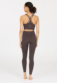 Braunes, geripptes Sportset mit einem trägerlosen Sport-BH und hochtaillierten Leggings, ausgestattet mit einer glatten Textur und dezenten Logo-Details.