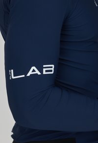 Langärmliges sportliches Shirt in Marineblau aus glattem, elastischem Material. Mit weißem "ELITE LAB"-Text auf dem linken Ärmel. Enganliegendes Design.