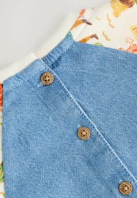 Chemise en denim avec un tissu bleu, dotée d'un empiècement à motifs floraux. Trois boutons en bois à l'arrière, col côtelé et texture douce.