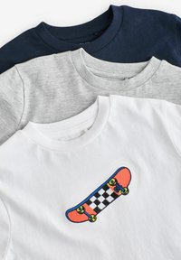 Drei T-Shirts: marineblau, grau und weiß. Das weiße Shirt hat eine gestickte orangefarbene Skateboard-Grafik mit einem karierter Muster. Aus Baumwollmaterial.