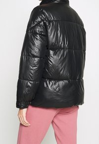 Černá puffer bunda vyrobená z lesklého, izolačního materiálu s vysokým límcem a elastickými manžetami, obsahuje viditelné prošívané části.