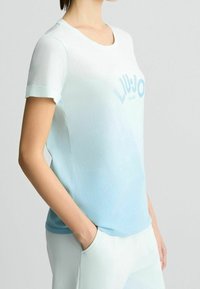 Camiseta de color azul claro con degradado, hecha de un tejido suave, que presenta un cuello redondo y mangas cortas, con el logotipo "LIU JO MILANO" en un detalle texturizado.