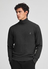 Maglione grigio scuro a collo alto realizzato in materiale morbido, con un design aderente, maniche lunghe e un piccolo logo sul petto.