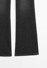 Pantalons évasés en denim noir avec une texture lisse, dotés d'une taille haute et de coutures contrastées le long des coutures.