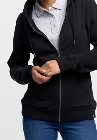 Felpa nera con zip dal tocco morbido, con colletto in grigio chiaro a contrasto tipico di una polo. Include tasche e polsini a coste.