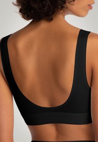 Reggiseno sportivo nero con spalline larghe, una profonda scollatura sulla schiena e tessuto testurizzato. Presenta una finitura liscia e un design senza cuciture.