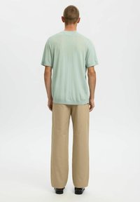 Chemise à manches courtes vert menthe clair avec un ourlet arrondi, associée à un pantalon beige à jambes larges. Texture lisse, design simple, sans motifs visibles.