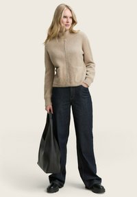 Beige textuur ge belegde ritstrui met lange mouwen, gecombineerd met donkere denim wijde pijpen jeans. Zwarte schoudertas en stevige zwarte schoenen inbegrepen.
