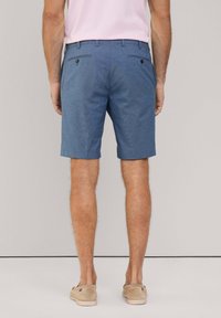 Shorts blu realizzati in tessuto testurizzato, dotati di due tasche posteriori con bottoni scuri. Abbinati a una camicia rosa chiaro e scarpe beige.