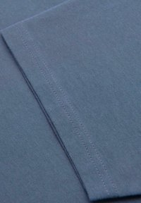 Gros plan sur un tissu bleu doux avec une double couture soignée le long d'un bord plié, mettant en valeur la texture et le détail de la couture.