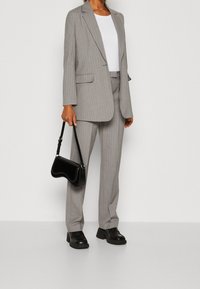 Traje gris a rayas con chaqueta y pantalones a medida, combinado con una blusa blanca y un bolso negro. Zapatos negros de tacón grueso.