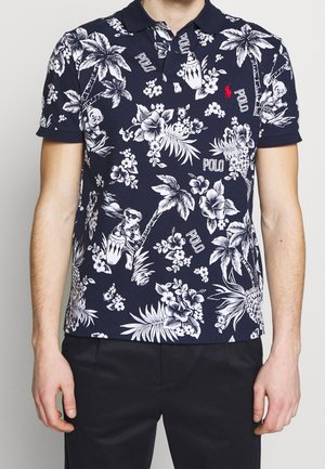 Granatowa koszulka polo z białym wzorem kwiatów i liści palmowych, z prążkowanym kołnierzykiem i krótkimi rękawami; zawiera akcenty z napisem "POLO".