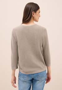 Hellgrauer gestrickter Pullover mit Rundhalsausschnitt und 3/4-Ärmeln, kombiniert mit hellblauen Jeans. Strukturierter Stoff und lockere Passform.