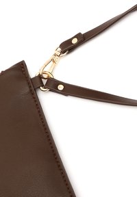 Hnedá kožená kabelka s detailmi rohu, zlatým uzáverom a nastaviteľným popruhom na bielom pozadí.
