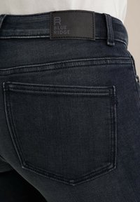 Sötét denim farmernadrág sima textúrával, fekete bőrcímmel a deréknál és klasszikus hátsó zsebből álló dizájnnal, finom varrással.