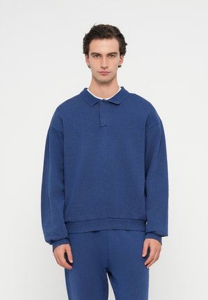 Blaues Sweatshirt aus Baumwolle mit klassischem Kragen, langen Ärmeln, gerippten Bündchen und Saum. Kombiniert mit passenden blauen Hosen. Einfaches, sauberes Design.