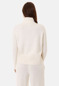 Maglione color crema con colletto alto a coste e orlo a coste. Tessuto a maglia con vestibilità comoda, abbinato a pantaloni coordinati in maglia.
