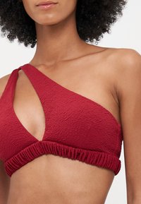 Sytě červený bikiny top na jedno rameno s texturovaným materiálem, který se vyznačuje vykrojeným designem a nařasením na spodním okraji.