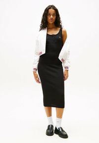Vestito midi nero a coste abbinato a un bomber corto bianco con righe rosse, calze bianche e mocassini neri.