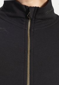 Black zip-up jacket featuring a high collar and a gold zipper. Fabric is smooth with visible seams and a subtle texture.