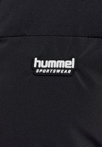 Sort sportstøjsstof med en tekstureret overflade. En hvid logo med teksten "hummel SPORTSWEAR" er tydeligt vist.