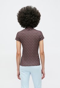 Priliehavá blúzka s krátkym rukávom v tmavohnedej farbe s geometrickým vzorom v červenej a krémovej farbe. Mäkká tkanina s hladkou textúrou, dizajn s vysokým golierom.