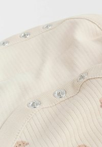 Chemise en tissu beige à côtes avec des boutons-pression en métal argenté et un subtil motif animal sur la partie avant.