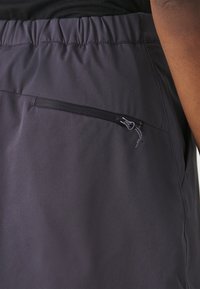 Donkergrijze sportshorts van zacht, lichtgewicht materiaal met een elastische tailleband en een ritszakje aan de zijkant.