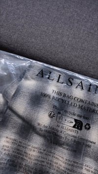 Transparante plastic tas met zwarte tekst, met het "ALLSAINTS" logo, recycling symbolen en verzorgingsinstructies. Tas gemaakt van 100% gerecycled materiaal.