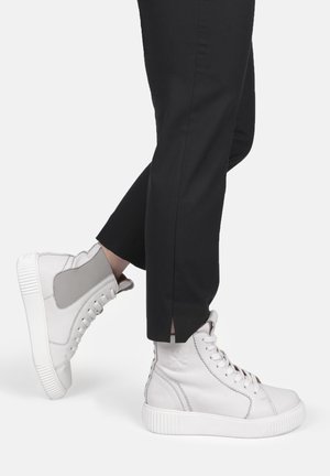 Weiße High-Top-Sneaker mit grauen Akzenten, aus glattem Leder, mit strukturiertem Außensohle und Schnürdesign. Getragen mit schwarzen schmalen Hosen.