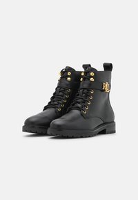 Botas de tobillo de cuero negro con herrajes en tono dorado, diseño con cordones y una correa decorativa con un logotipo. Suela de goma duradera.