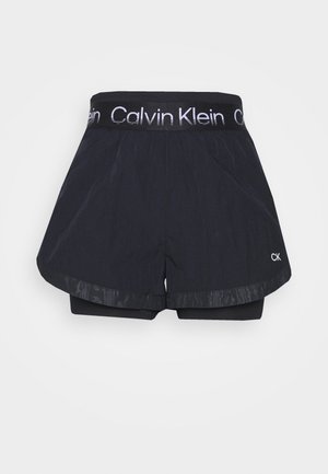 Shorts de sport noirs Calvin Klein avec ceinture élastique, texte de logo blanc et design en tissu superposé avec petites initiales CK sur la jambe.